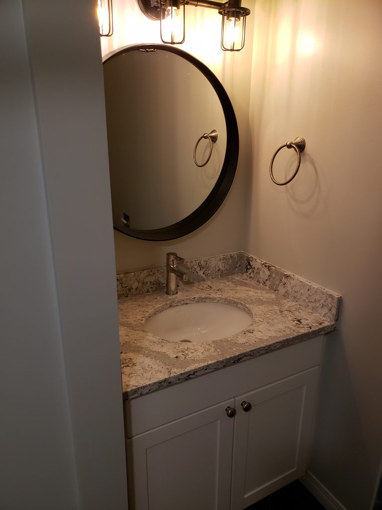 Cambria quartz countertop, a simple Kohler undermount sink, and a single lever Moen set of taps. An oval mirror and a wall mounted vanity light.